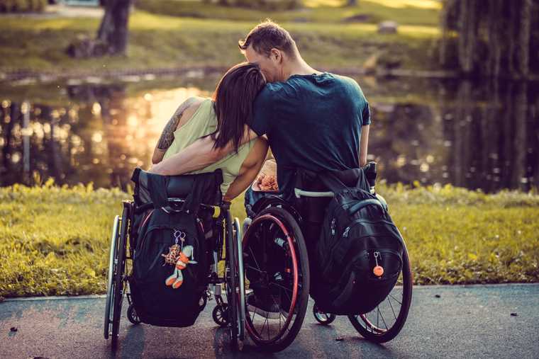 Young couple in wheelchairs, enjoying a sunset view on the bank of a pond