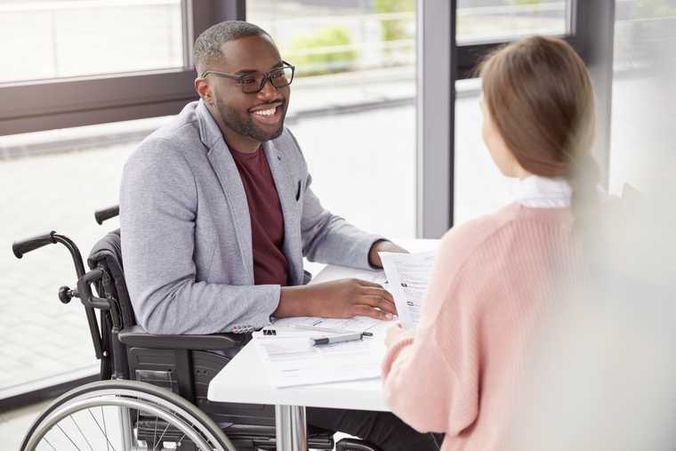 young man in wheelchair sits at table with a woman holding pape