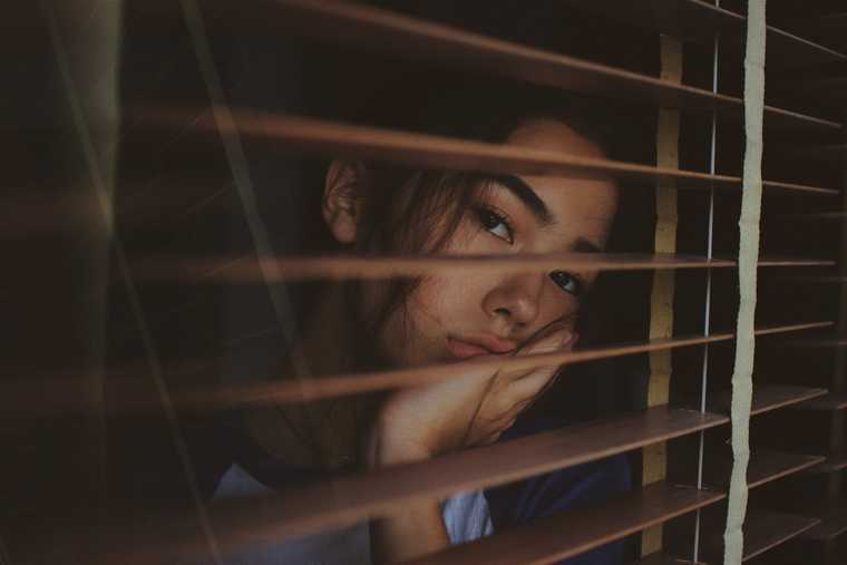 Woman sadly looking through blinds