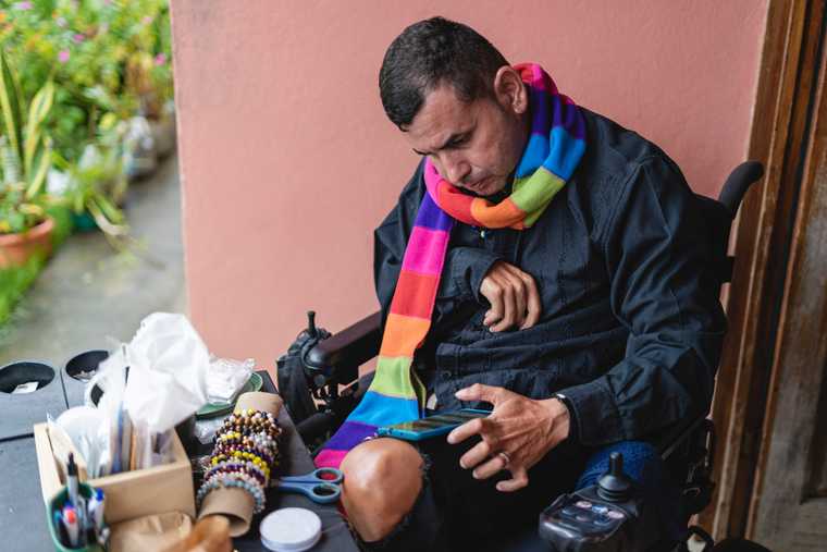 man in a powered wheelchair and limited dexerity uses a cell phone on his knee with one hand